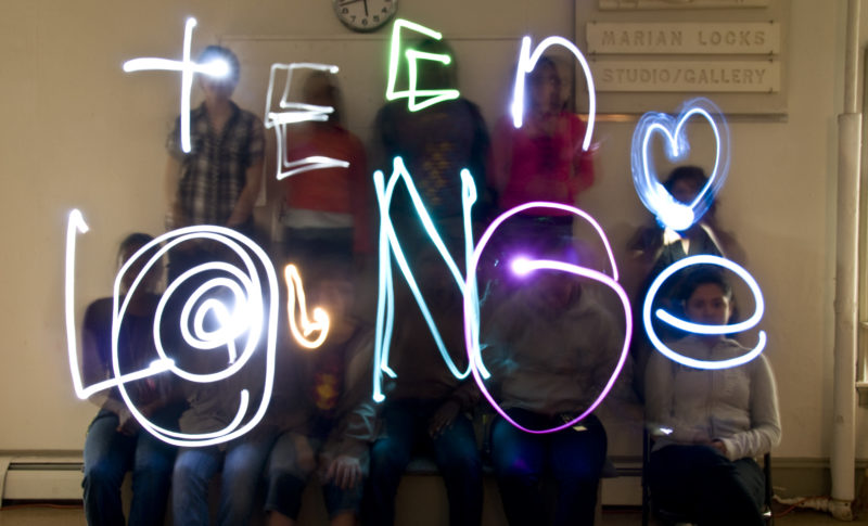 the words "teen lounge" written in glowing lights in front of a group of young people